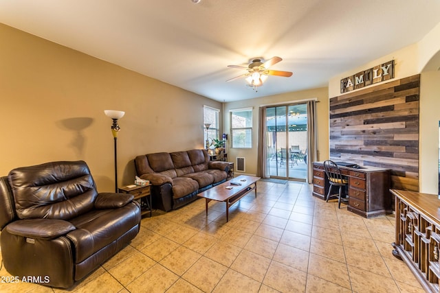 living room with ceiling fan, wood walls, and light tile patterned floors