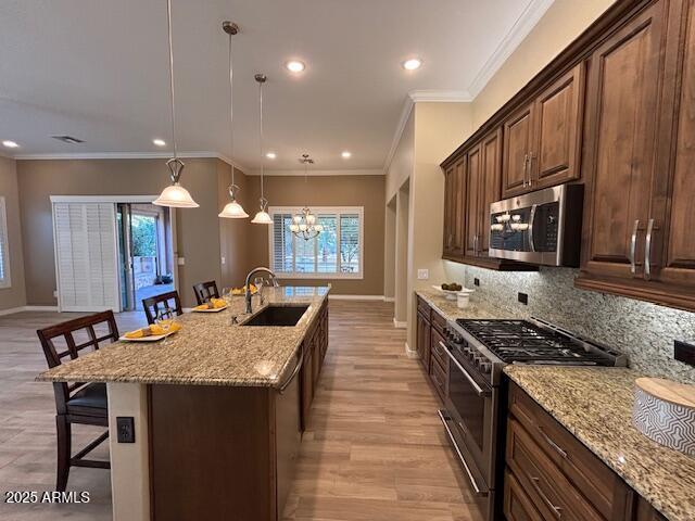 kitchen with a kitchen bar, sink, hanging light fixtures, appliances with stainless steel finishes, and an island with sink