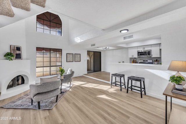 living area with a fireplace with raised hearth, baseboards, visible vents, and light wood-style floors