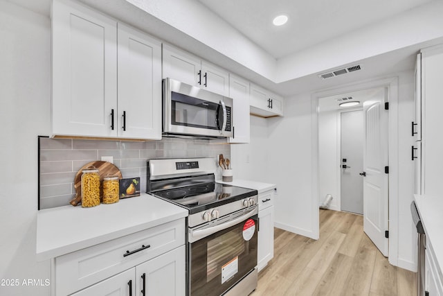 kitchen featuring light wood finished floors, stainless steel appliances, visible vents, decorative backsplash, and white cabinets