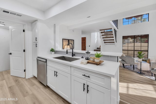 kitchen featuring visible vents, a peninsula, a sink, light wood-type flooring, and stainless steel dishwasher