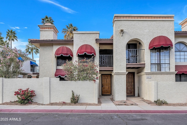 view of front of home with a tiled roof, fence, a balcony, and stucco siding