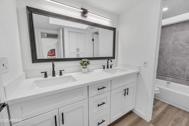 full bath featuring double vanity, wood finished floors, a sink, and toilet