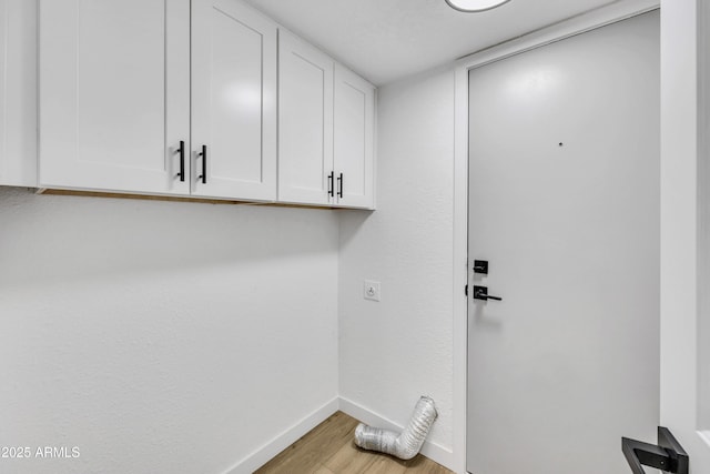 washroom with cabinet space, electric dryer hookup, baseboards, and light wood-style floors