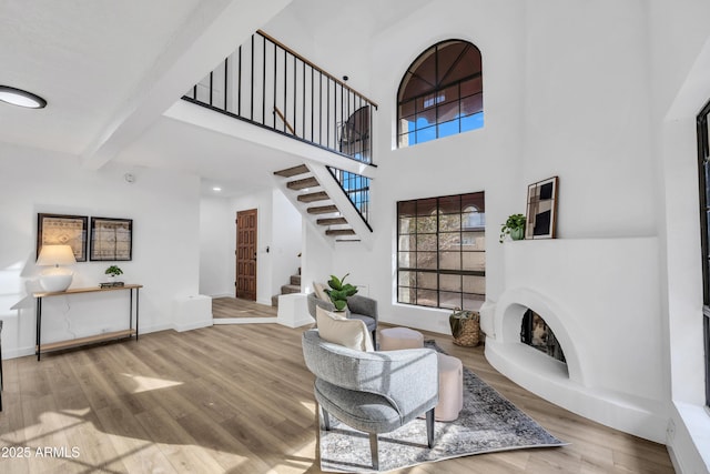 living room with a fireplace with raised hearth, wood finished floors, baseboards, stairway, and beam ceiling