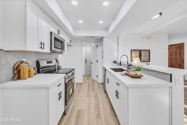 kitchen featuring a sink, stainless steel appliances, light countertops, light wood-type flooring, and backsplash