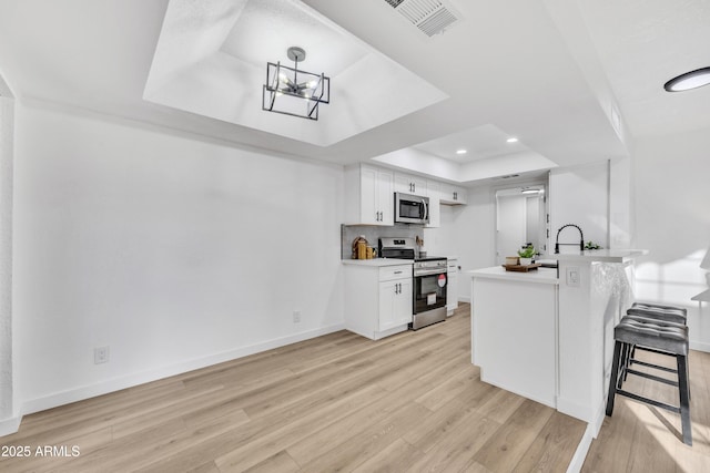 kitchen featuring a peninsula, visible vents, appliances with stainless steel finishes, light wood finished floors, and a raised ceiling