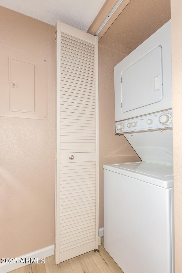 washroom with stacked washer and dryer, laundry area, baseboards, light wood-type flooring, and electric panel