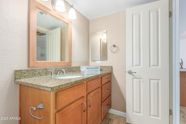 bathroom featuring baseboards, visible vents, wood finished floors, and vanity