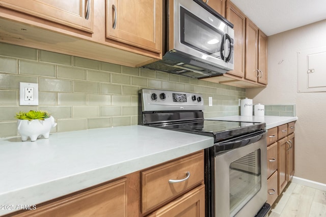 kitchen with light wood-style flooring, stainless steel appliances, light countertops, backsplash, and brown cabinetry