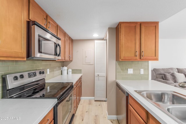 kitchen featuring stainless steel appliances, a sink, light wood-style floors, light countertops, and brown cabinets