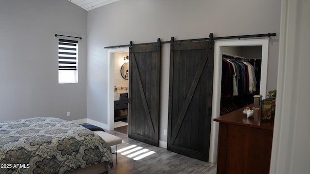 bedroom featuring wood-type flooring, a barn door, and connected bathroom