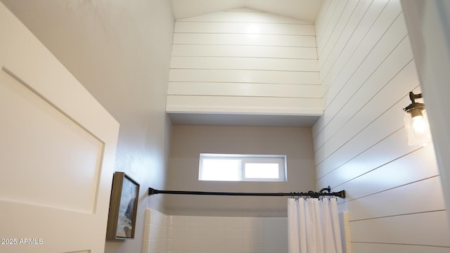 interior space with vaulted ceiling, wooden walls, and walk in shower