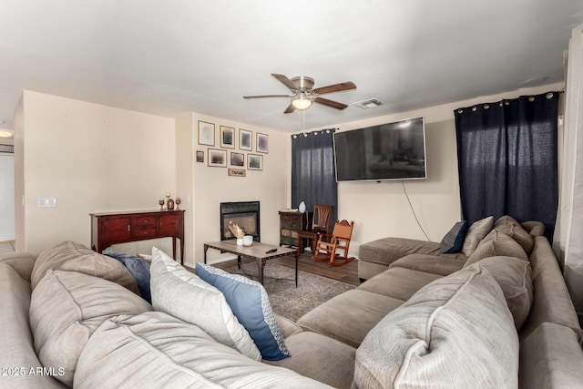 living room featuring a ceiling fan, visible vents, a glass covered fireplace, and wood finished floors