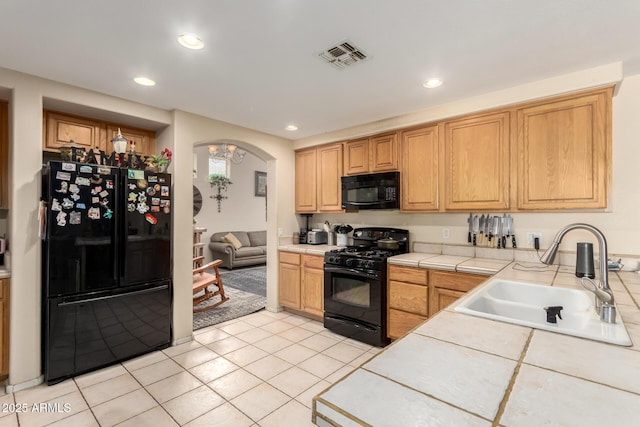 kitchen featuring a sink, tile counters, visible vents, black appliances, and arched walkways