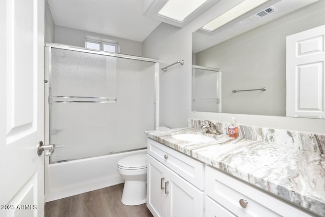 full bathroom featuring vanity, hardwood / wood-style floors, shower / bath combination with glass door, and toilet