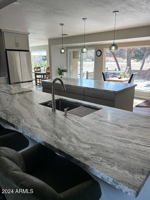 kitchen with stainless steel refrigerator, sink, a center island with sink, and pendant lighting