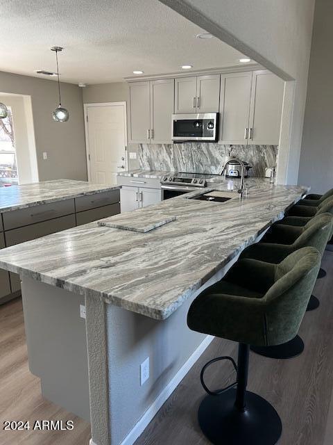 kitchen featuring light stone counters, decorative light fixtures, appliances with stainless steel finishes, a kitchen breakfast bar, and backsplash