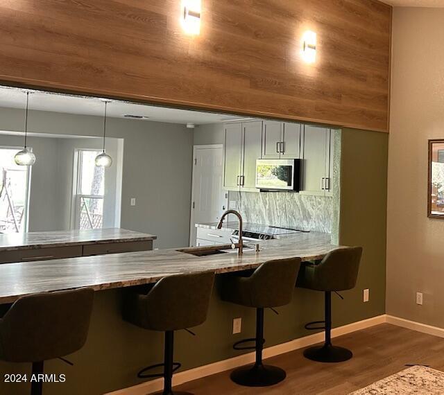 kitchen featuring sink, hanging light fixtures, a kitchen breakfast bar, hardwood / wood-style flooring, and decorative backsplash