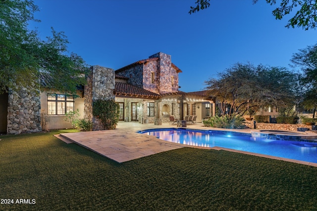 rear view of house with a yard, a patio, stucco siding, and stone siding