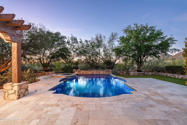 pool at dusk with a patio and an in ground hot tub