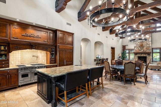 kitchen with a high ceiling, a stone fireplace, an island with sink, high end appliances, and light stone counters