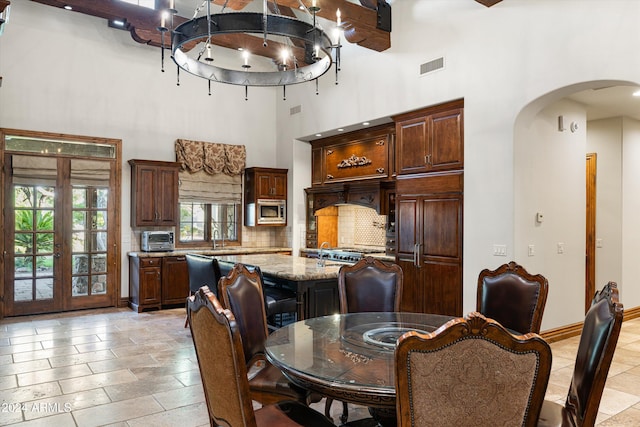 dining space featuring french doors, beam ceiling, sink, a chandelier, and a towering ceiling