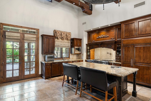 kitchen featuring a kitchen island with sink, built in appliances, a kitchen bar, plenty of natural light, and a towering ceiling