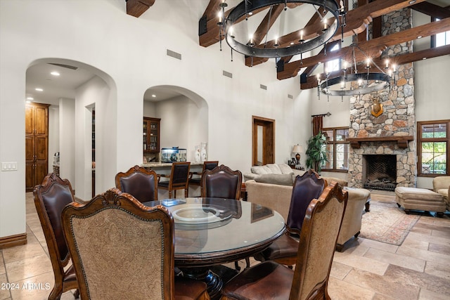 dining room with a stone fireplace, a chandelier, a high ceiling, and beamed ceiling