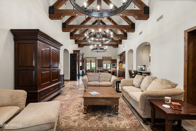 living room featuring a notable chandelier, visible vents, a towering ceiling, beamed ceiling, and arched walkways