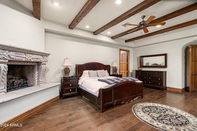 bedroom featuring baseboards, a high end fireplace, hardwood / wood-style flooring, arched walkways, and beamed ceiling