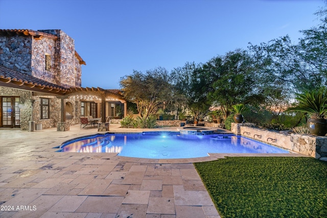 pool at dusk with an in ground hot tub, pool water feature, and a patio