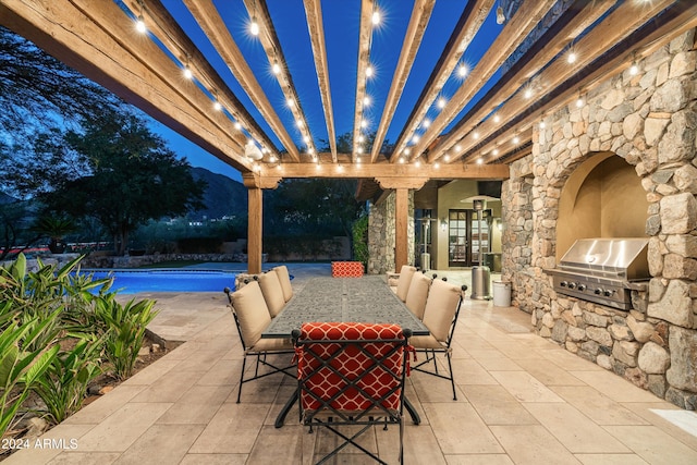 patio at twilight with an outdoor kitchen, a grill, and a pergola