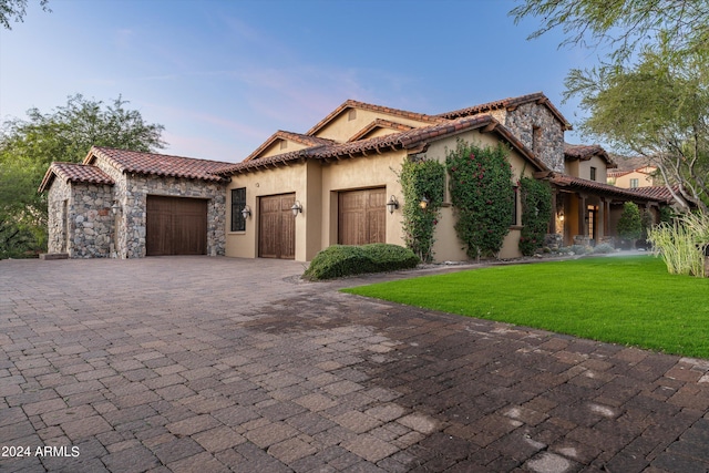 mediterranean / spanish-style house with a garage, stucco siding, a tiled roof, a front lawn, and decorative driveway