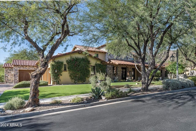 mediterranean / spanish home with a garage, stucco siding, a tile roof, a front lawn, and driveway