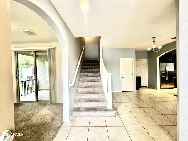 staircase with baseboards, a chandelier, tile patterned flooring, carpet floors, and visible vents