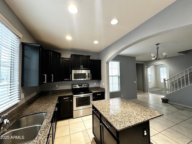 kitchen with light tile patterned floors, arched walkways, a sink, dark cabinetry, and stainless steel appliances