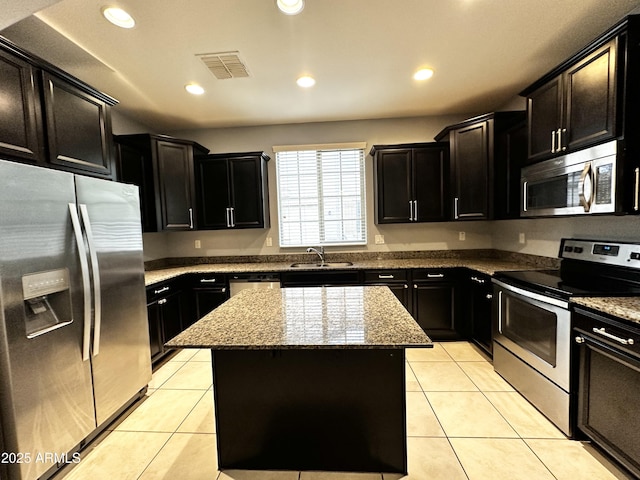 kitchen with a center island, light stone countertops, visible vents, dark cabinetry, and stainless steel appliances