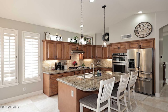 kitchen with a center island with sink, sink, stone countertops, a kitchen bar, and stainless steel appliances