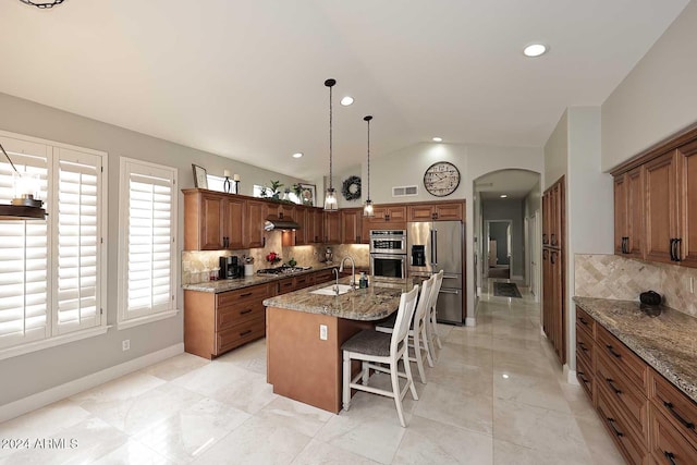 kitchen featuring light stone countertops, sink, an island with sink, vaulted ceiling, and appliances with stainless steel finishes