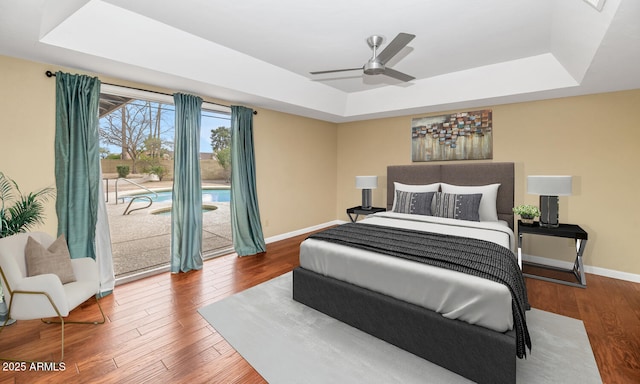 bedroom with access to exterior, a raised ceiling, baseboards, and wood finished floors