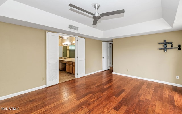 unfurnished bedroom featuring a raised ceiling, visible vents, baseboards, and wood finished floors