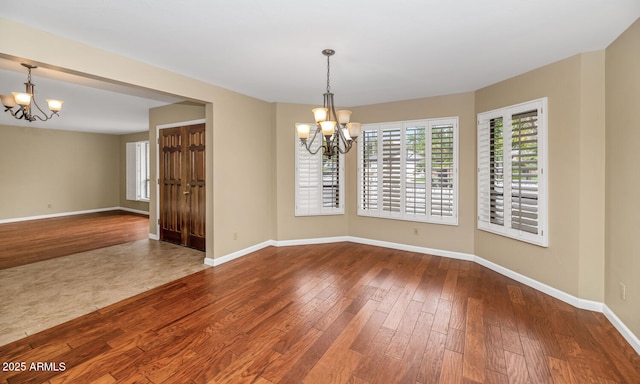 empty room with baseboards, wood finished floors, and a notable chandelier