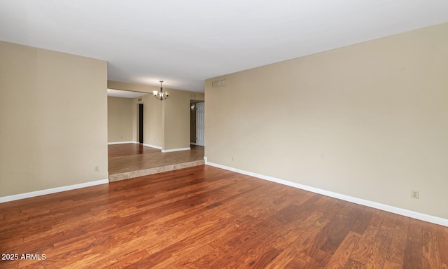 spare room featuring baseboards, wood finished floors, and a notable chandelier