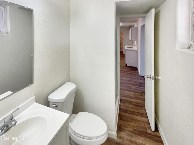 half bath featuring toilet, vanity, wood finished floors, and baseboards