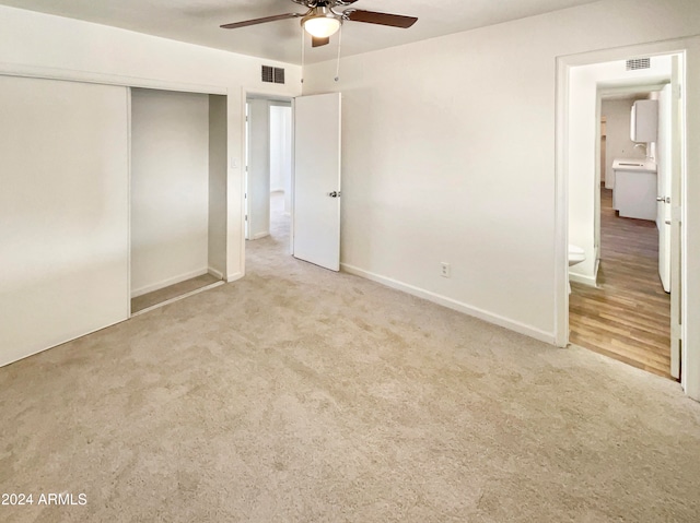 unfurnished bedroom featuring light carpet, a closet, ensuite bath, and ceiling fan