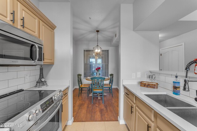 kitchen with sink, appliances with stainless steel finishes, light brown cabinets, light tile patterned floors, and an inviting chandelier