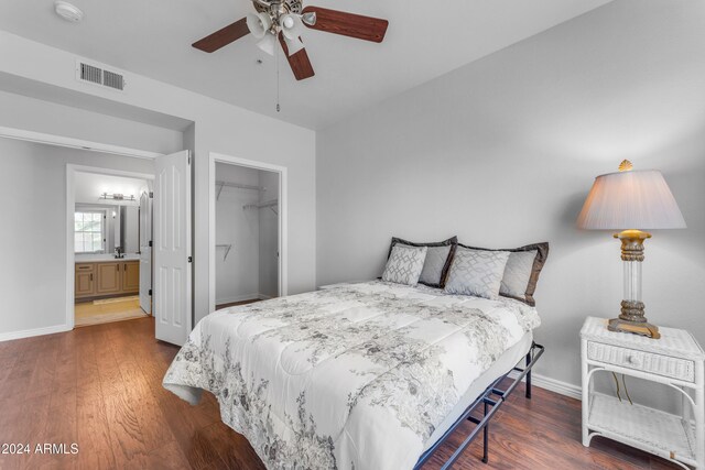 bedroom with a closet, a spacious closet, connected bathroom, dark hardwood / wood-style flooring, and ceiling fan