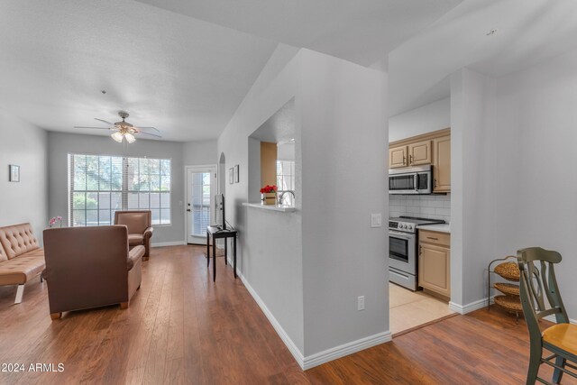 interior space with light hardwood / wood-style floors, appliances with stainless steel finishes, light brown cabinetry, ceiling fan, and decorative backsplash