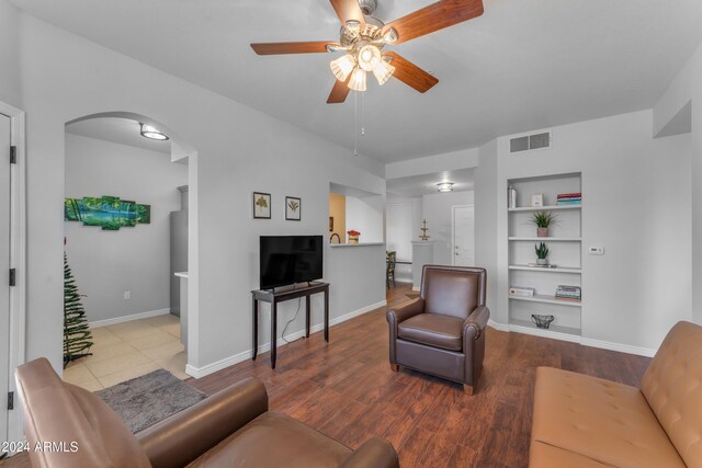 living room featuring built in shelves, hardwood / wood-style flooring, and ceiling fan